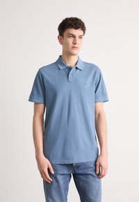 Polo shirt albastru deschis din bumbac, cu guler, placă cu două butoane, mâneci scurte și un logo brodat subtil pe piept.