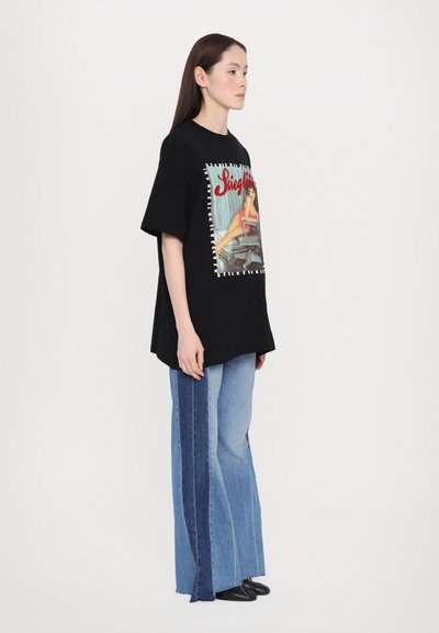 Camiseta negra de gran tamaño con un estampado gráfico colorido, combinada con jeans de un azul claro que tienen paneles laterales de un azul oscuro y un corte de pierna ancha.