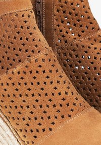 Botín de ante marrón con diseño perforado, cierre de cremallera y suela de yute al estilo espadrille. Cuenta con una textura suave y sutiles acentos de costura.