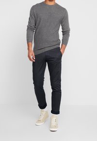 Gray textured sweater, dark slim-fit denim pants, and beige high-top sneakers with white laces, set against a plain white background.