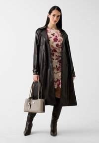 Schwarzer Ledermantel über einem geblümten, plissierten Kleid. Das Outfit umfasst kniehohe braune Stiefel und eine hellgraue Handtasche mit Logo.