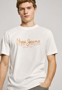 Biele bavlnené tričko s oranžovým textovým logom "Pepe Jeans" s dekoratívnymi prvkami. Krátke rukávy a okrúhly výstrih. Jednoduchý dizajn.