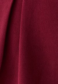 Tela burdeos con una superficie suave y texturizada, que presenta sutiles variaciones de tono y un acabado liso, cayendo en pliegues suaves.