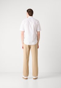 Camisa blanca de manga corta con una textura suave, combinada con pantalones beige de corte holgado y zapatos blancos con acentos marrones.