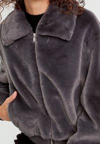Gray faux fur jacket with a collar, front zipper, and ribbed cuffs. Soft, plush texture with a fitted silhouette.