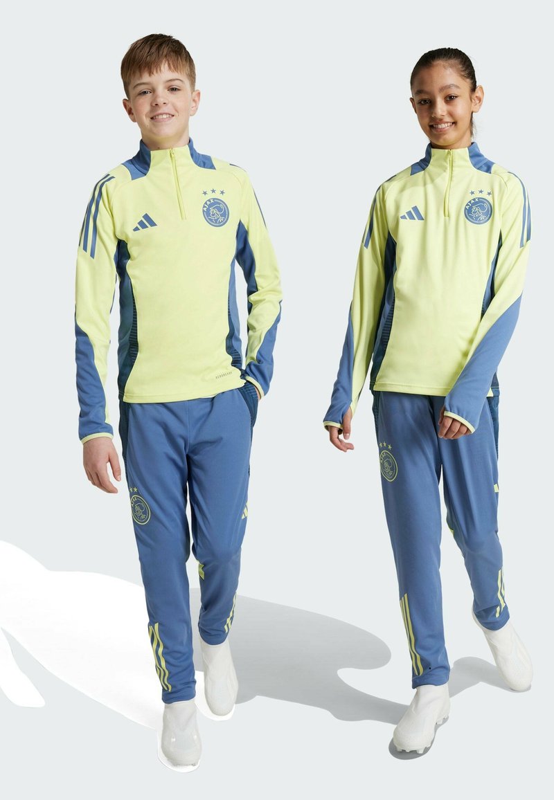Adidas ungdoms träningsdräkter med en ljusgul överdel med blå detaljer och matchande blå byxor. Innehåller logotyper och ränder på ärmar och sidor.