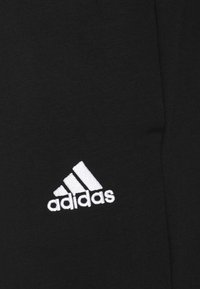 Schwarze Sporthose mit glatter Textur und tailliertem Design; zeigt ein weißes, gesticktes Adidas-Logo auf der unteren linken Seite.