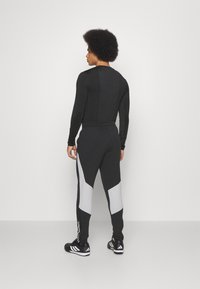 Schwarzes Sportoberteil mit langen Ärmeln und enganliegenden Hosen mit grauen Akzenten. Das Design zeichnet sich durch eine schlanke, athletische Passform und strukturierte Stoffe aus.