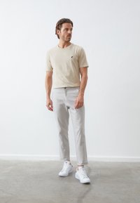 Világos bézs póló, rövid ujjal, kerek nyakkivágással, kis fekete logóval. Világosszürke nadrág, slim fit. Fehér sneaker, minimalista dizájn.