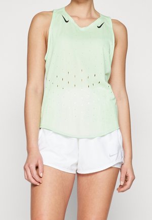 Person iført en lysegrøn ærmeløs Nike tanktop med perforeringer og hvide Nike-shorts, synlige fra nakken til midt på låret.