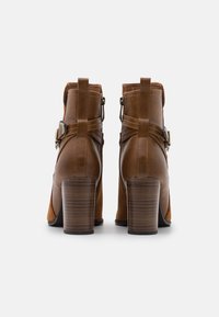 Bottes cuir marron à cheville avec un talon haut en bois, des détails de sangles et un mélange de textures lisses et en suède.