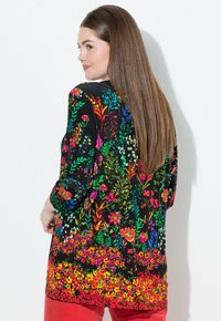 Schwarze Tunika mit einem lebhaften Blumenmuster in Rot, Rosa, Blau und Grün auf der Rückseite, mit langen Ärmeln und einem lockeren, fließenden Design.