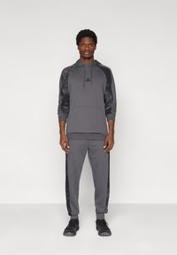 Γκρι αθλητικό φούτερ με κουκούλα, με μαύρα μανίκια με σχέδιο και τσέπη μπροστά, συνδυασμένο με αντίστοιχο στενό παντελόνι φόρμας.