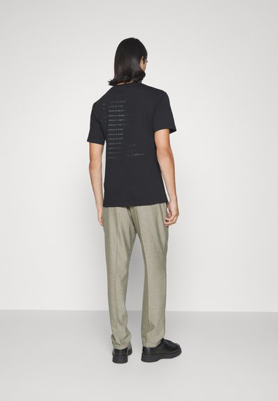 Black T-shirt with text on the back, paired with light grey plaid trousers and black shoes. Simple design, cotton material.