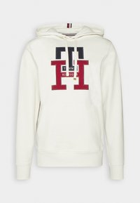 Sweat à capuche blanc avec grand logo Tommy Hilfiger noir et rouge sur le devant, capuche à cordon de serrage et poche kangourou frontale.