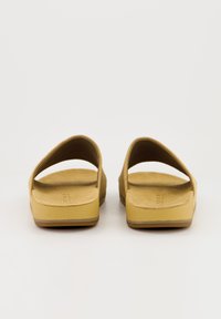 Sandales en daim jaune au design minimaliste, avec un dos ouvert et une semelle intérieure texturée, se caractérisant par une semelle plateforme basse et sans matériel visible.