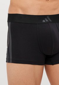 Schwarze Boxer-Shorts aus weichem Stoff, mit einem breiten schwarzen Bund, seitlichen Streifen in einem dunkleren Farbton und einer körperbetonten Passform.