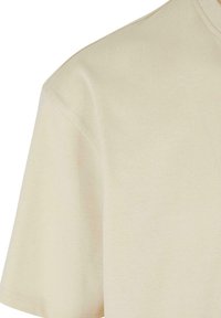 Tricou din bumbac bej, cu o textură ușoară și fină. Dispune de un guler clasic rotund și mâneci scurte, cu accente subtile de cusătură.