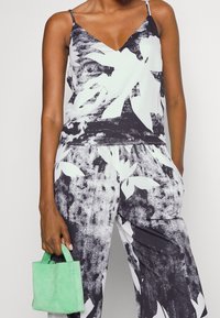 Top senza maniche in bianco e nero con stampa floreale, scollatura a V e vestibilità ampia, abbinato a pantaloni coordinati. Tieni in mano una piccola borsa verde.