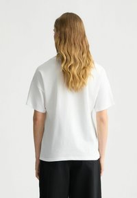 T-shirt bianco in cotone con maniche corte, vestibilità comoda e design semplice. Nessun motivo o grafica visibile sul retro.