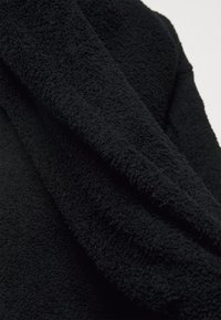 Tissu en polaire noire douce montrant une surface dense et texturée avec de petites boucles, plié pour mettre en valeur son épaisseur et sa douceur.