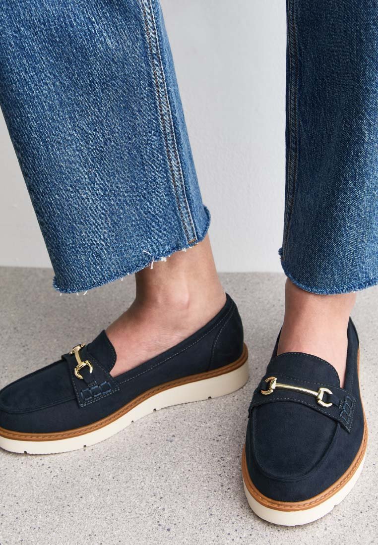 Mocassins en daim bleu marine avec un bout rond, des accents en métal doré et une semelle texturée de couleur crème. Portés avec un denim coupé.