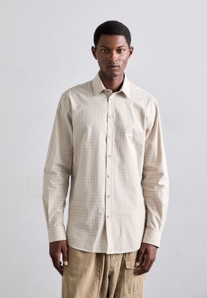 Cămașă bej deschis, tip button-up, cu un model în carouri, mâneci lungi, textură moale și nasturi albaștri. Purtată cu pantaloni kaki.