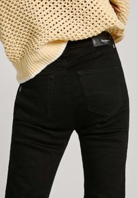 Vaqueros pitillo negros con bolsillos traseros y costuras contrastantes, combinados con un suéter amarillo de punto con dobladillo acanalado.