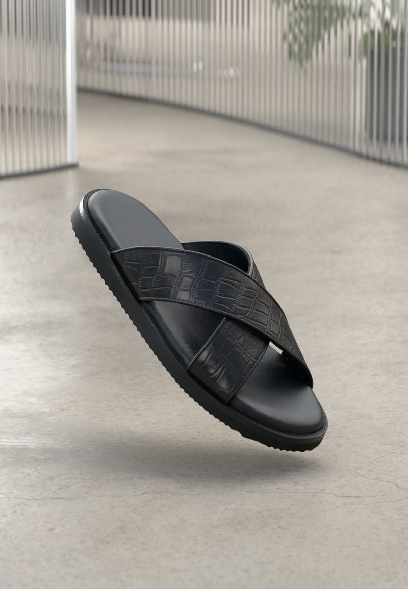 Sandales noires avec une surface lisse et brillante, et des brides texturées ornées d'un motif crocodile. Semelle plate, design minimaliste.