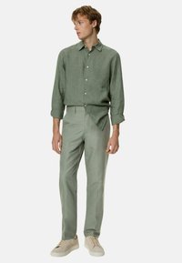 Lichtgroen linnen shirt met button-down kraag, lange mouwen en opgerolde boorden, gecombineerd met lichtgroene op maat gemaakte broeken en beige sneakers.