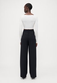 Hvit langermet crop topp kombinert med vide svarte bukser, med elastisk midjebånd og to baklommer, glatt tekstur.