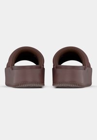 Καφέ PVC τσόκαρα με στρογγυλεμένη πίσω πλευρά και λεία επιφάνεια. Διαθέτουν παχιά, υφή σόλα και ανοιχτό σχεδιασμό· μινιμαλιστικό και στυλ που φοριέται εύκολα.