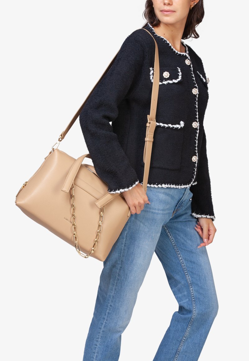 Beige læderhåndtaske med kædeakcent, glat tekstur og struktureret design. Bæres med en marineblå sweater med hvid kant og lommer.