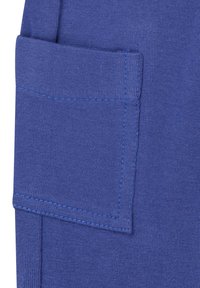 Poche en tissu bleu sur un vêtement, présentant une couture surélevée et une finition texturée. La couleur est uniforme avec des détails de couture contrastants.