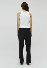 Zwarte elastische taillebroek gecombineerd met een witte, getailleerde tanktop. De stof lijkt zacht en lichtgewicht, geschikt voor casual kleding.