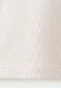 Gros plan d’un tissu blanc côtelé avec des coutures visibles le long de l'ourlet.