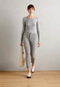 Grå, ribbet langermet topp kombinert med matchende tapered bukser med et teksturert mønster, og hvite slip-on sko. Modellen holder en kremfarget tote-bag.