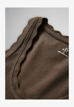 Tuvplāns brūnai ribotai auduma daļai ar viļņotu malu un baltu drukātu etiķeti ar tekstu "The Set, M, Made in Bangladesh."