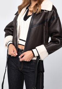 Brun konstläderjacka med shearling-krage och manschetter, dragkedja fram, svarta läderdetaljer och en ribbad stickad tröja under.