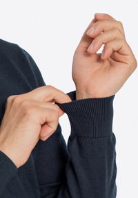 Ciemnoniebieski sweter z prążkowanymi mankietami, charakteryzujący się gładką fakturą. Ręce dostosowują rękaw, podkreślając dopasowanie i jakość.