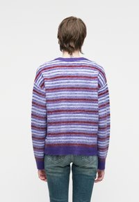 Fioletowy sweter w paski o różnych szerokościach jasnofioletowego, ciemnofioletowego i czerwonego koloru. Miękka, puszysta tekstura oraz prążkowane mankiety i dół.