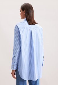 Camicia a righe blu chiaro e bianco con un plissè sul retro, vestibilità casual, maniche lunghe e orlo arrotondato, dotata di polsini con bottoni e tessuto morbido.