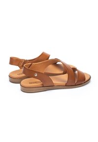 Sandalias de cuero marrón con tiras cruzadas y tira trasera, que cuentan con una suela plana y un discreto detalle de marca en la plantilla.