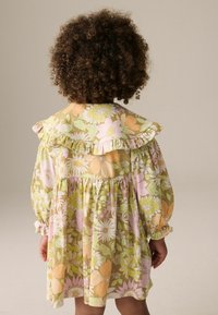 Blumenkleid mit einem grünen, rosa und orangefarbenen Muster, Rüschenspiegel und langen Ärmeln. Aus leichtem Stoff mit lockerer Passform gefertigt.