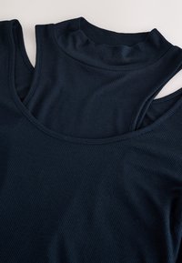 Top in tessuto a coste blu navy scuro con scollo rotondo e design a strati. Presenta una texture morbida e spalle scoperte, che valorizzano la silhouette.