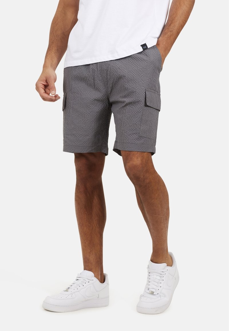 Szare szorty cargo z teksturowanym wzorem, z dwiema bocznymi kieszeniami i luźnym krojem, w komplecie z białymi trampkami i białym t-shirtem.