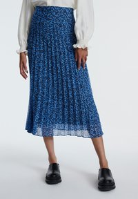 Blaue plissierte Midirock mit schwarzem Blumenmuster, transparenter Textur und einem gerafften Taillenbund, kombiniert mit schwarzen Slippern.