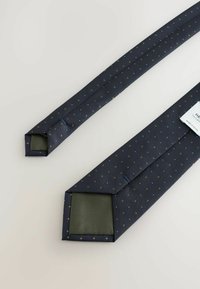 Marinefarbener Krawatte mit kleinen weißen und olivgrünen Punkten, aus strukturiertem Stoff gefertigt, mit einer einfarbigen grünen Unterseite und einem quadratischen Enddesign.