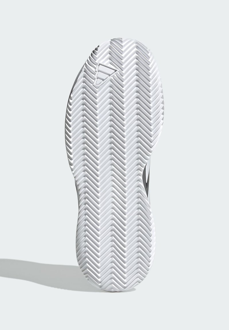 Schuhsohle mit einem weißen Gummi-Design, das ein Zickzackprofil für besseren Halt aufweist. Beinhaltet ein Logo in der Nähe der Zehenpartie und hat glatte Kanten.
