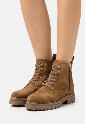 Bruna mockaankelboots med rund tå, snörning framtill, guldfärgade öljetter, sidodragkedja och en kraftig, texturerad gummisula.